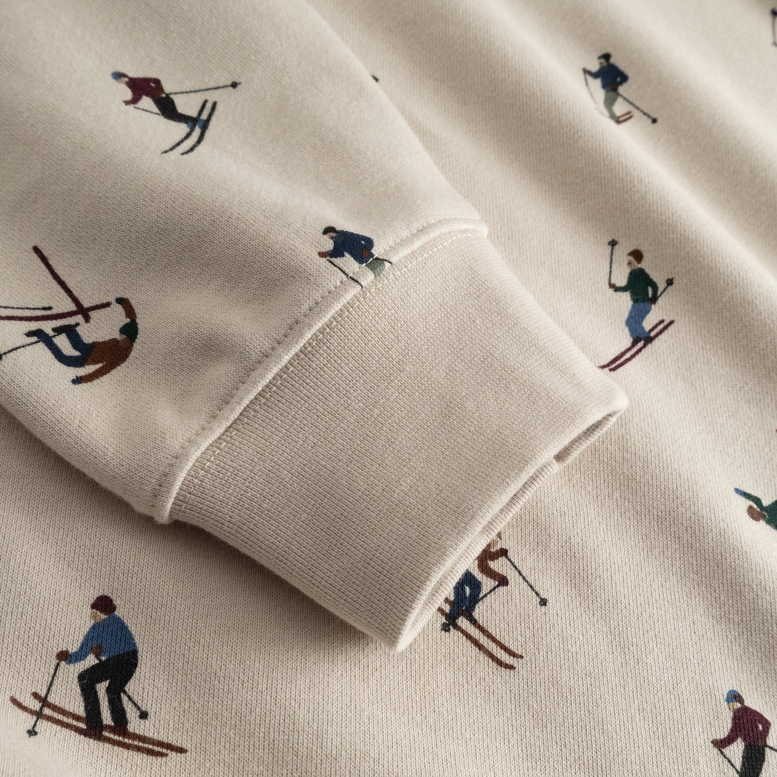 A detailed look at the sleeve of the oat white Falun Ski Team hoodie, featuring its fun all-over skier print.