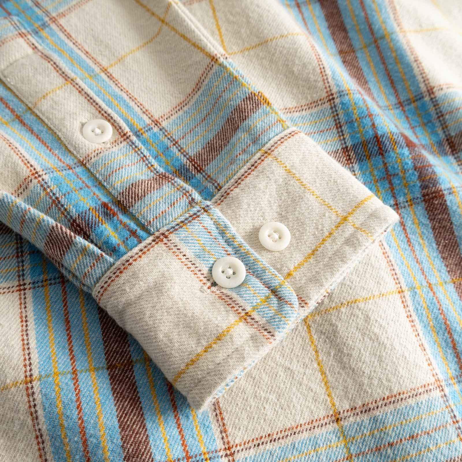 Gros plan sur le poignet en flanelle douce de la chemise Rute, aux carreaux tartan blanc avoine, bleu et marron.