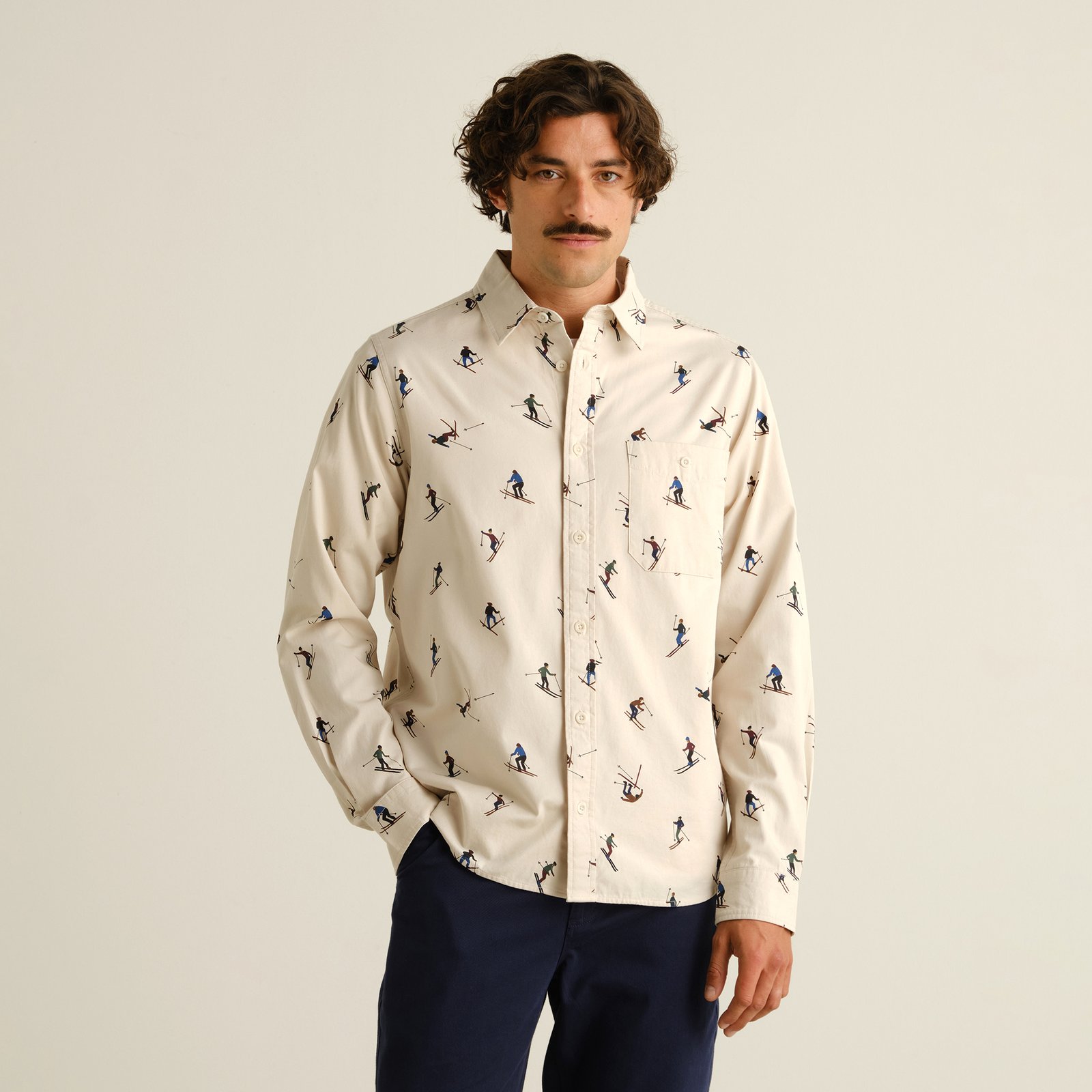 A man models the Shirt Lunnevik Ski Team in Oat White, a relaxed-fit shirt with a playful all-over skier print.