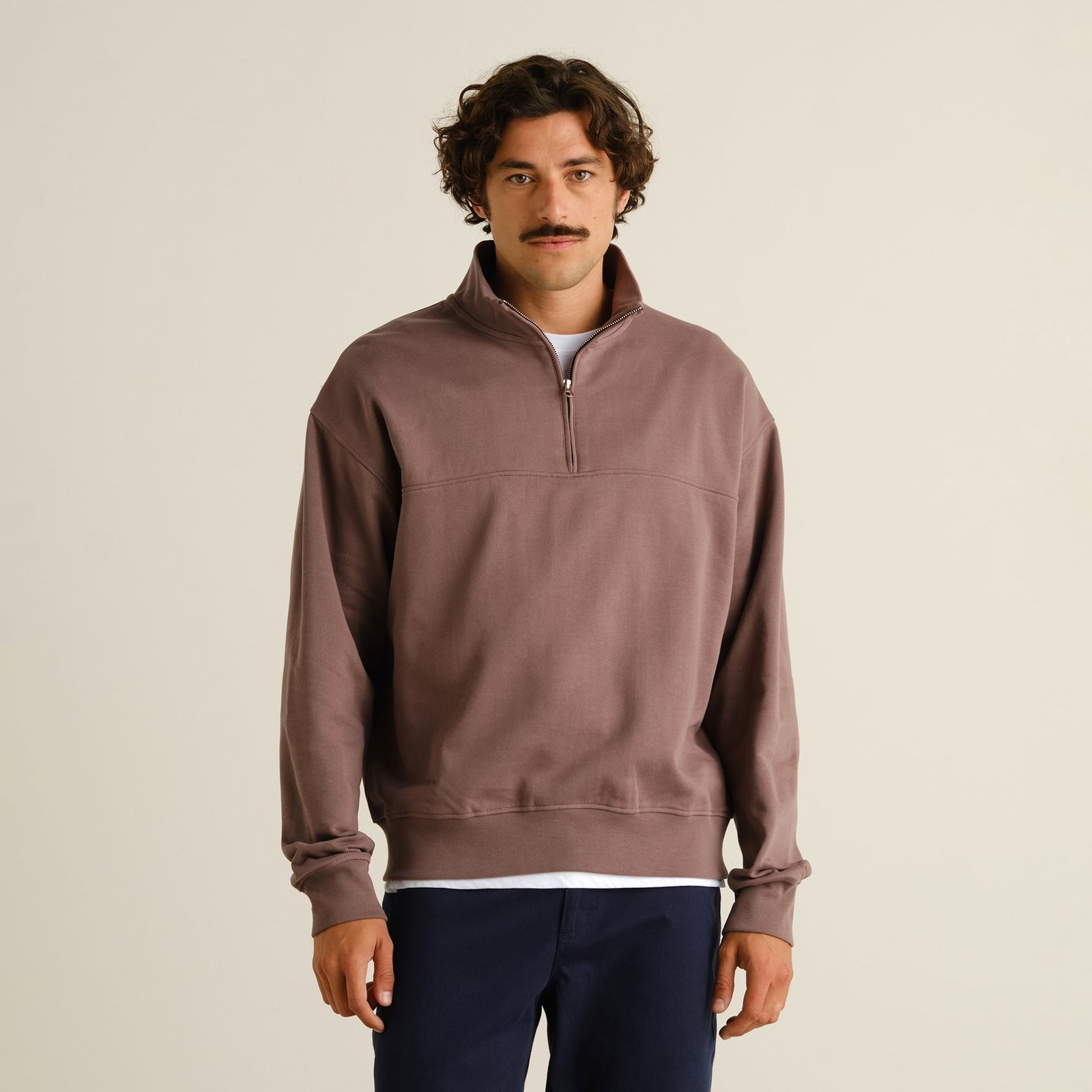 A man looks at the camera while wearing the relaxed-fit Half Zip Sweatshirt Sandvalla in Sparrow Brown.