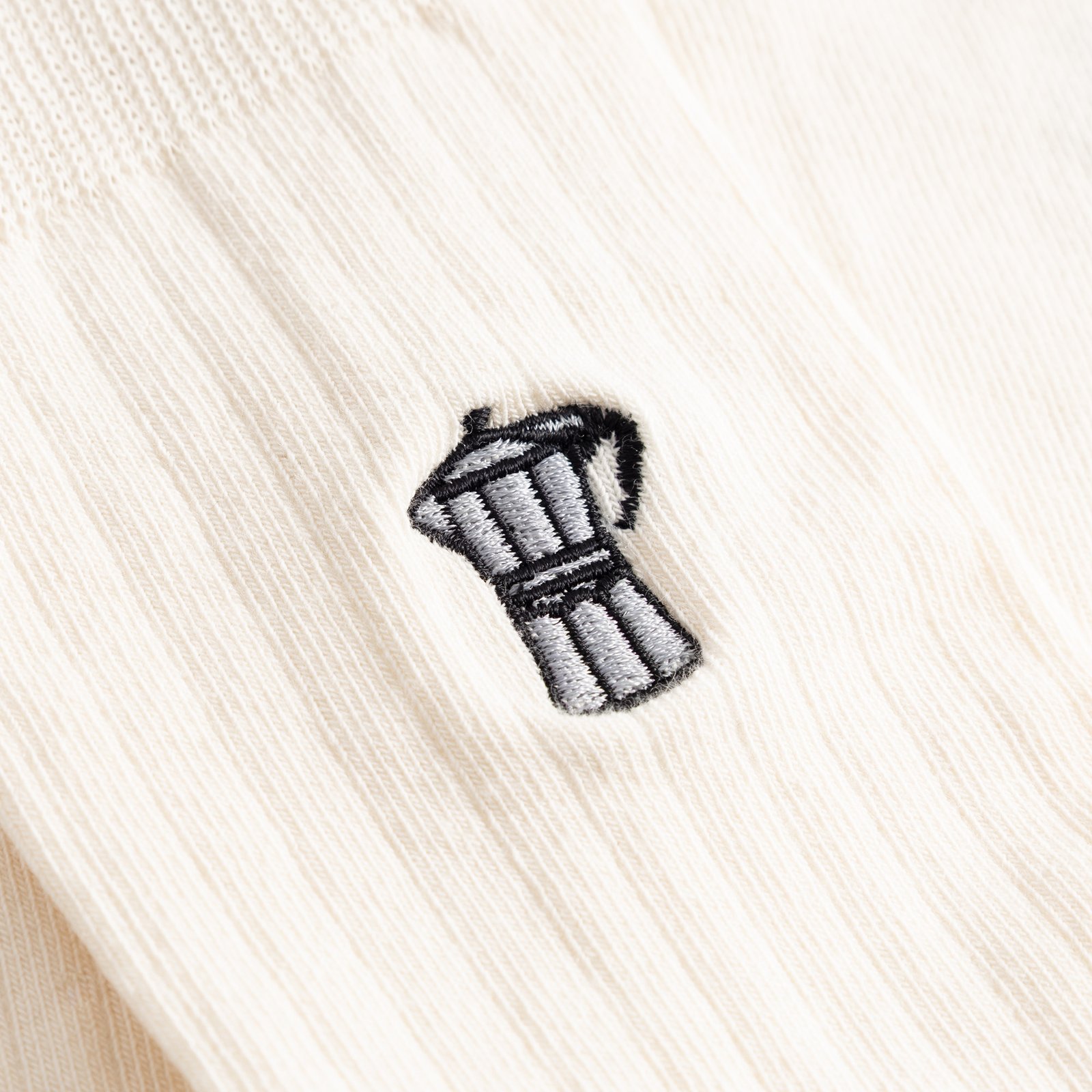 A detailed close-up of the small moka pot embroidered onto the ribbed fabric of the off-white Dedicated Knivsta socks.
