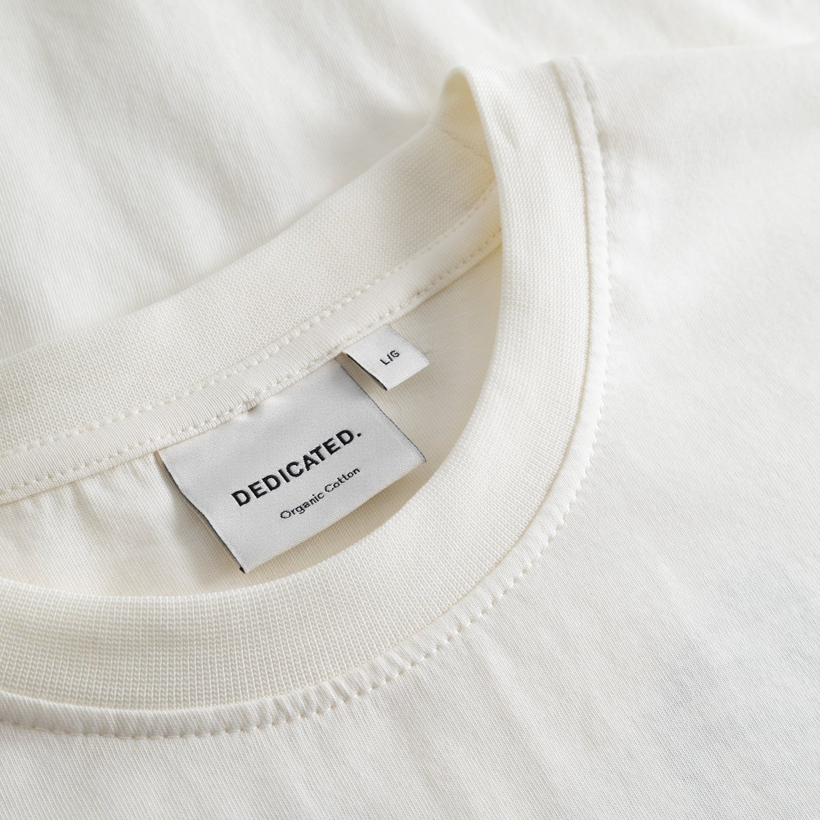 A detailed close-up of the ribbed crew neck and brand label on the off-white T-shirt Stockholm Camp Crew.