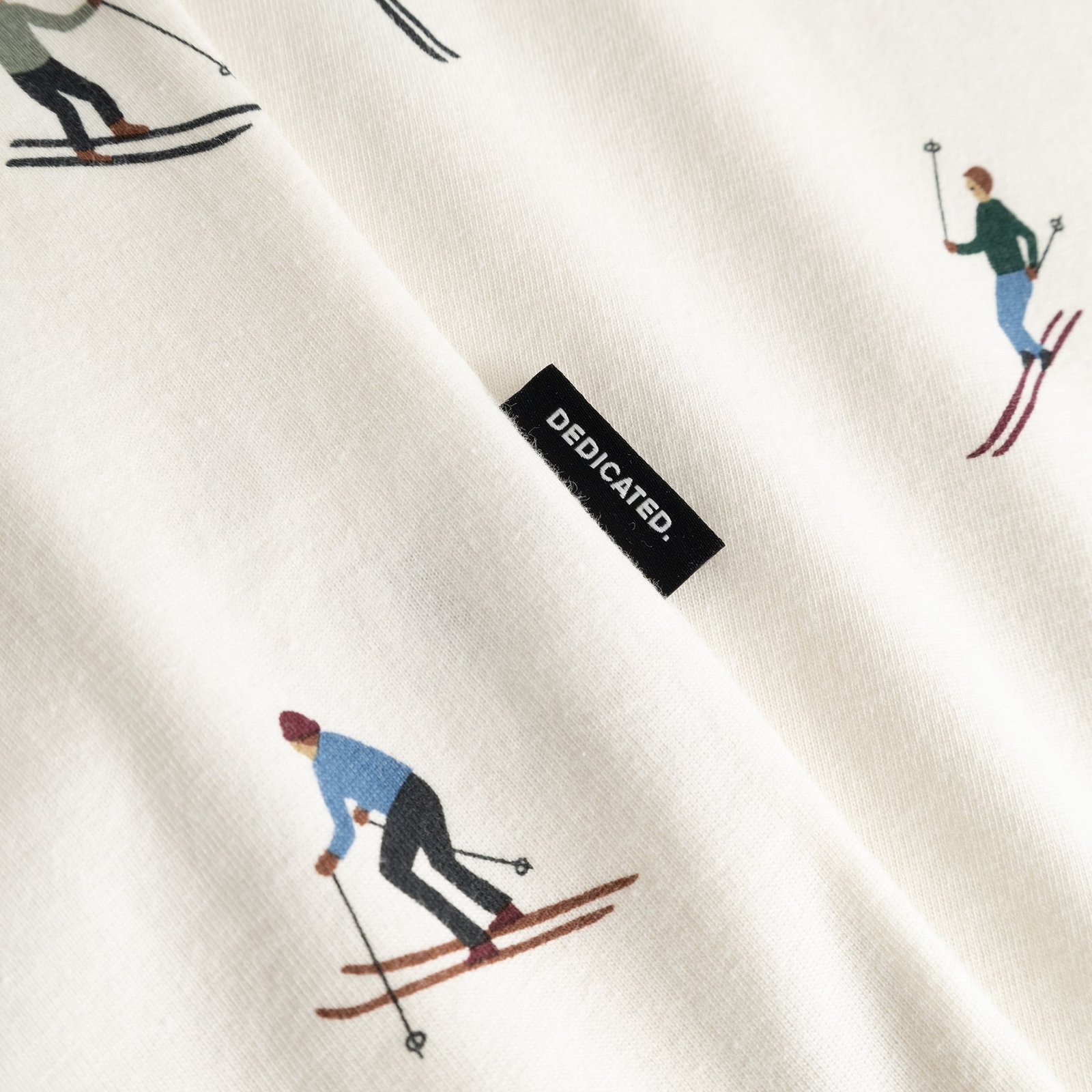 A close-up of the off-white Stockholm Ski Team t-shirt's fabric, showing the skier print and Dedicated brand tag.