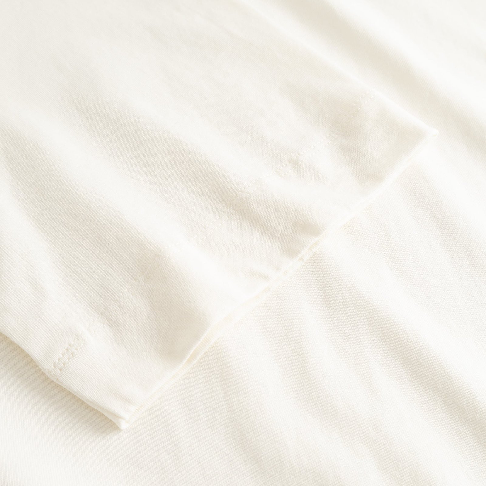 Close-up of the finely stitched sleeve on the T-shirt Vadstena in soft, off-white organic cotton.