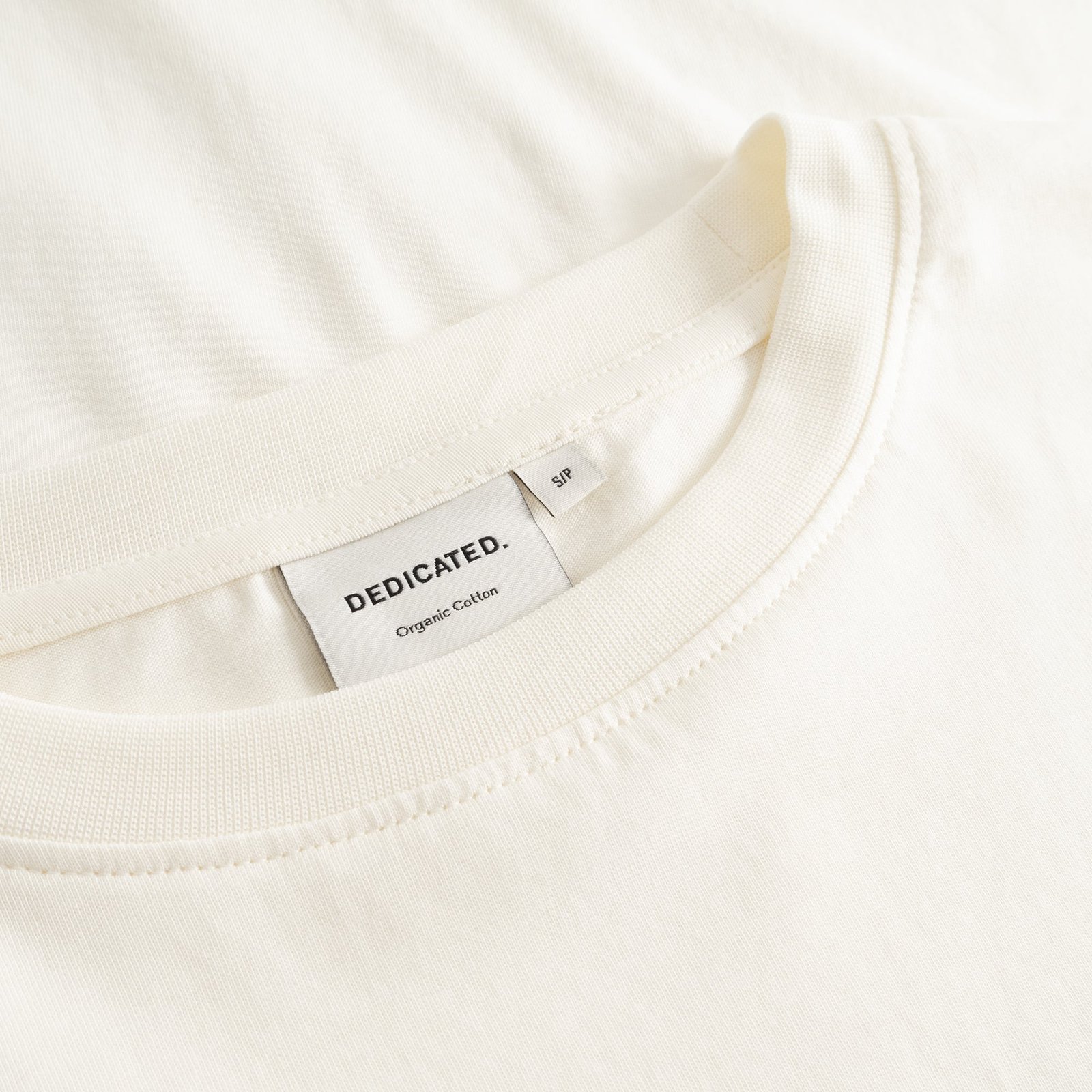 Close-up of the ribbed collar and Dedicated brand label on the off-white organic cotton T-shirt Vadstena.