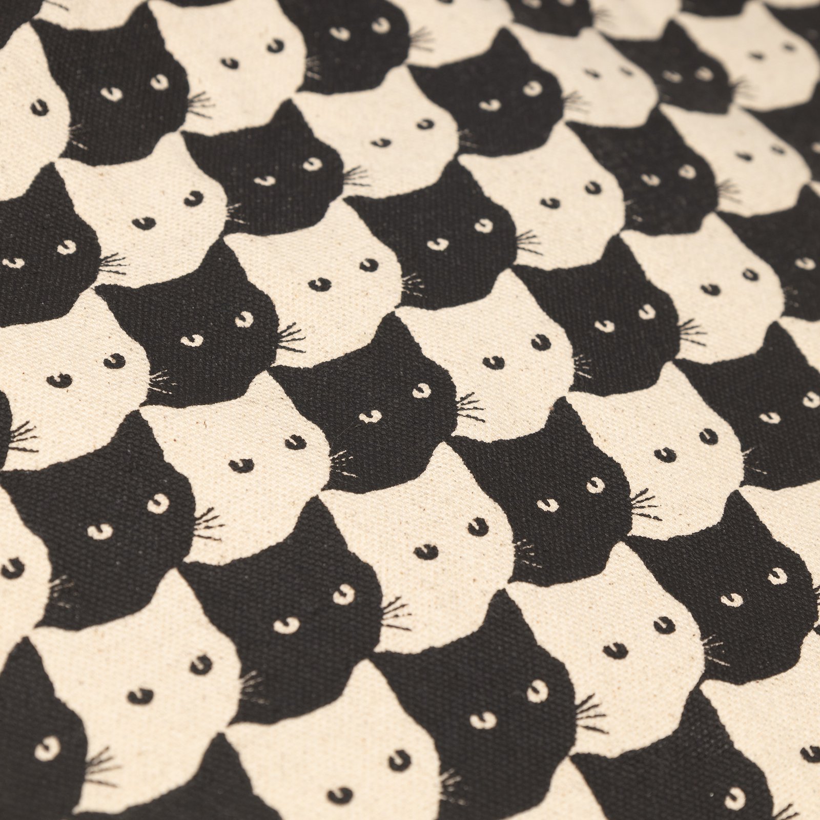Close-up of the Tote Bag Torekov's sturdy canvas, featuring a playful, interlocking pattern of black and off-white cat faces.