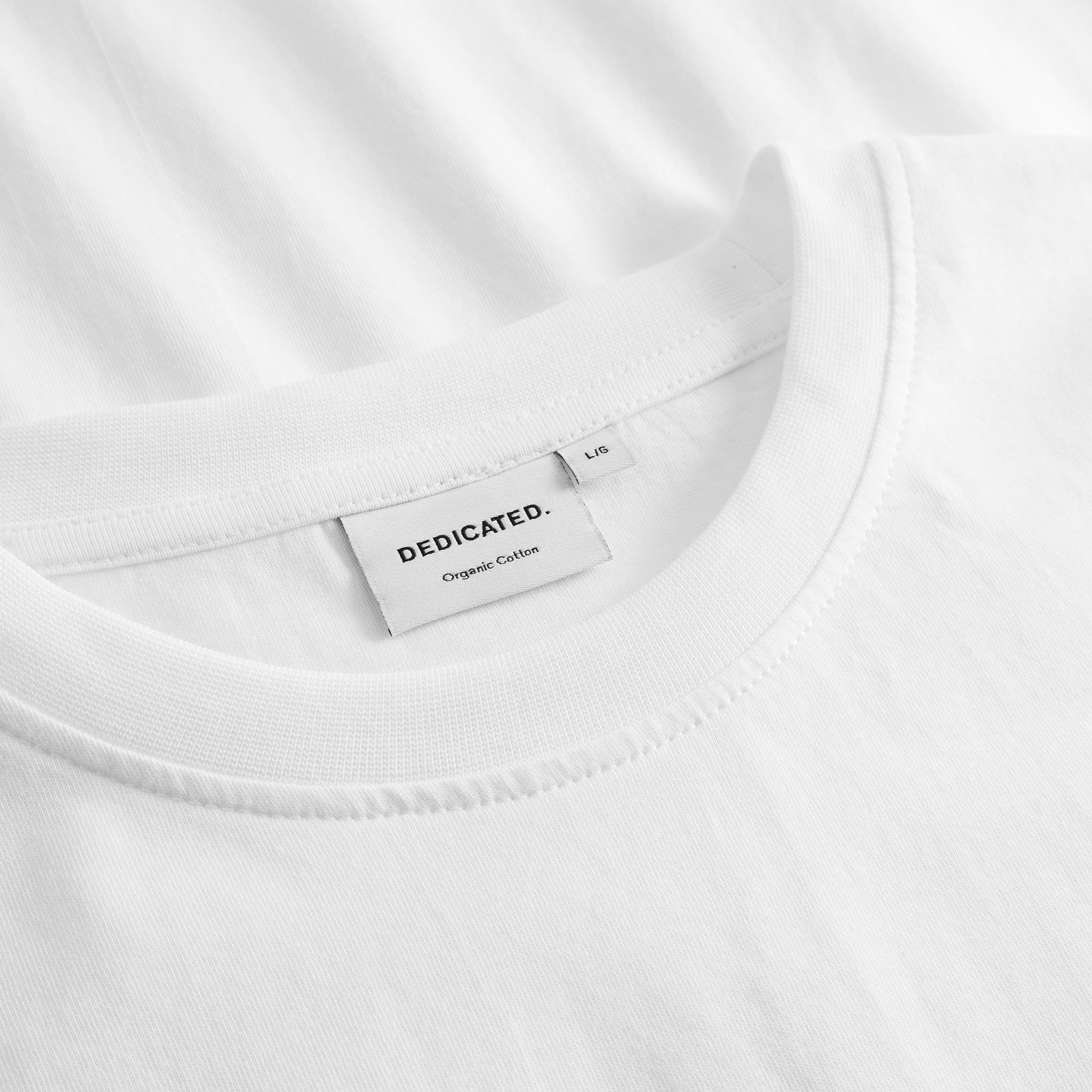 Close-up detail of the ribbed neckline and Dedicated brand label inside the white Stockholm Ski Crash EMB t-shirt.
