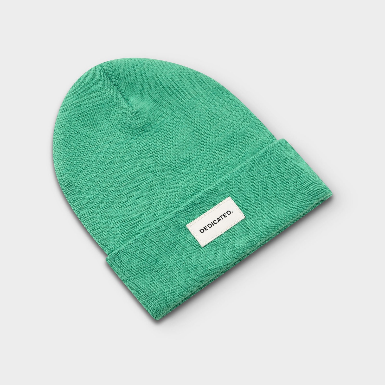 Dedicated Beanie Kiruna i Winter Green, plattlagd i en studiobild. Mössan har ett brett uppvik med en logotyp.