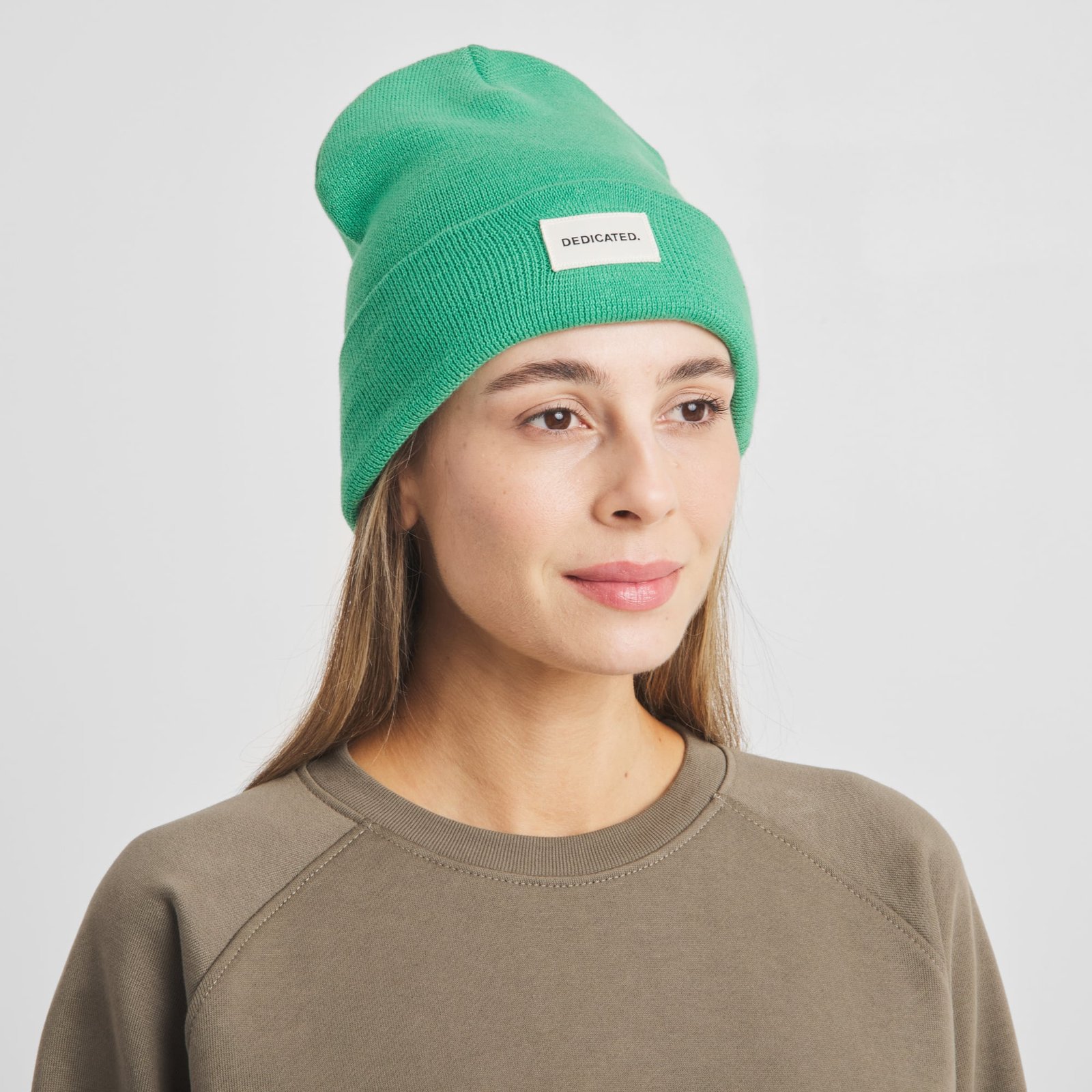En kvinna ler mjukt i den klargröna mössan Beanie Kiruna Winter Green.