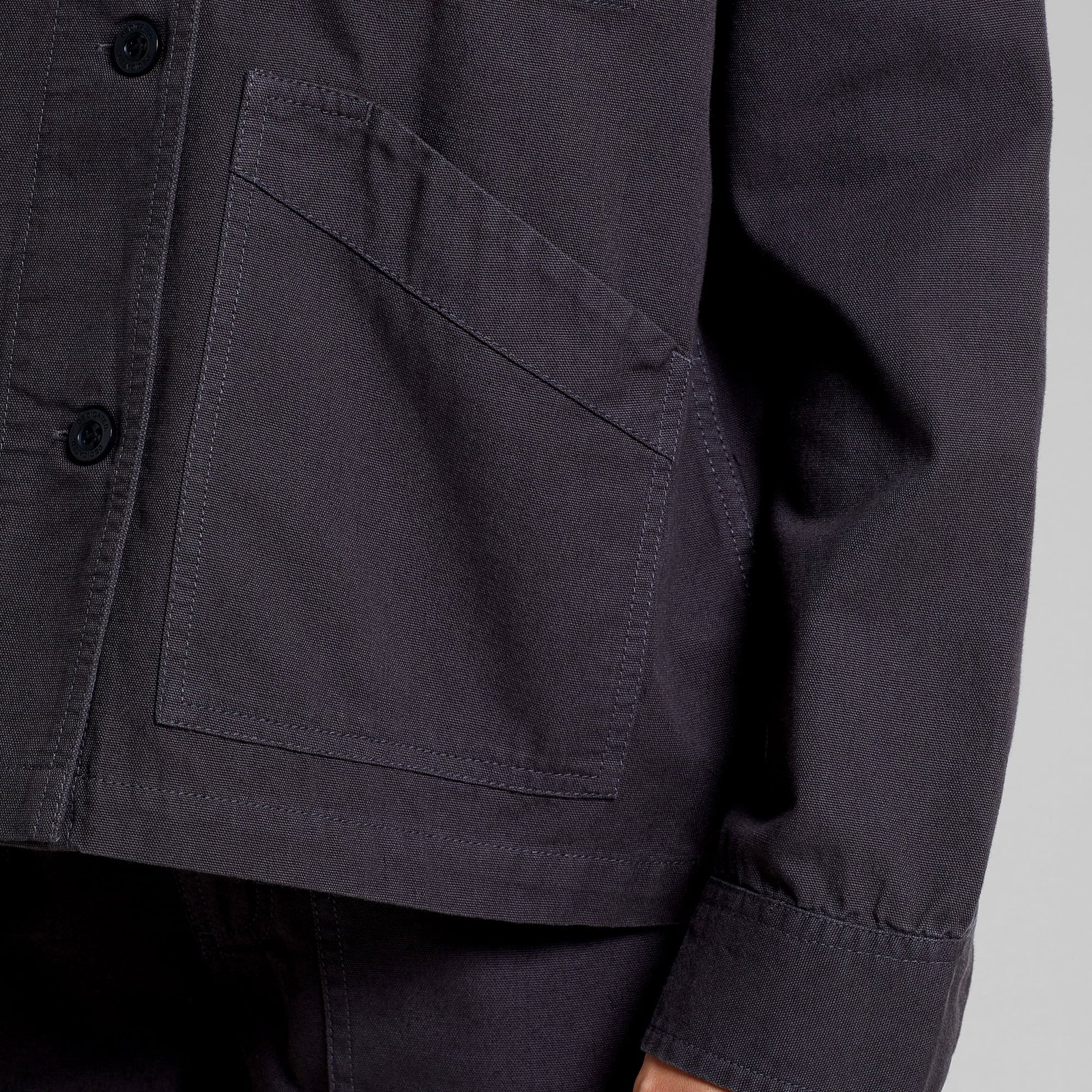 Close-up detail shot of the Stiby Canvas Jacket in Phantom Black, focusing on the angled front pocket and buttoned cuff.