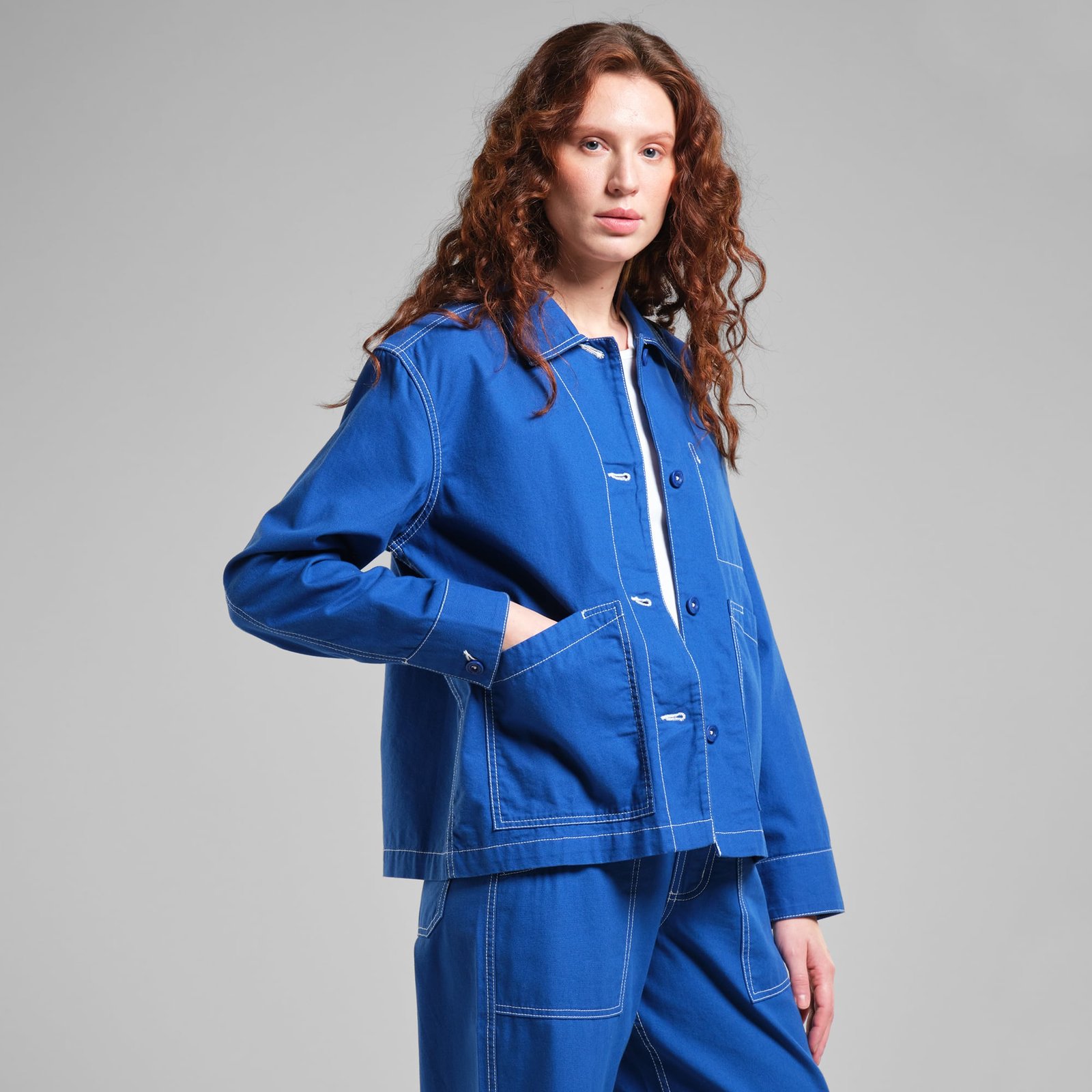 A woman with long curly hair models the bright blue Stiby Canvas Jacket, posing with her hand in her pocket.