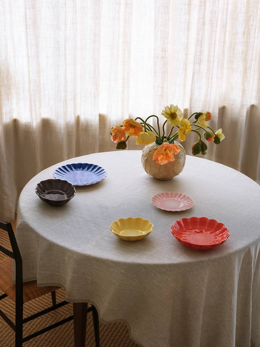 Round table setting with five small hand-painted bowls in different colours by Mateus, placed on a light linen table cloth with a flower vase in the centre.