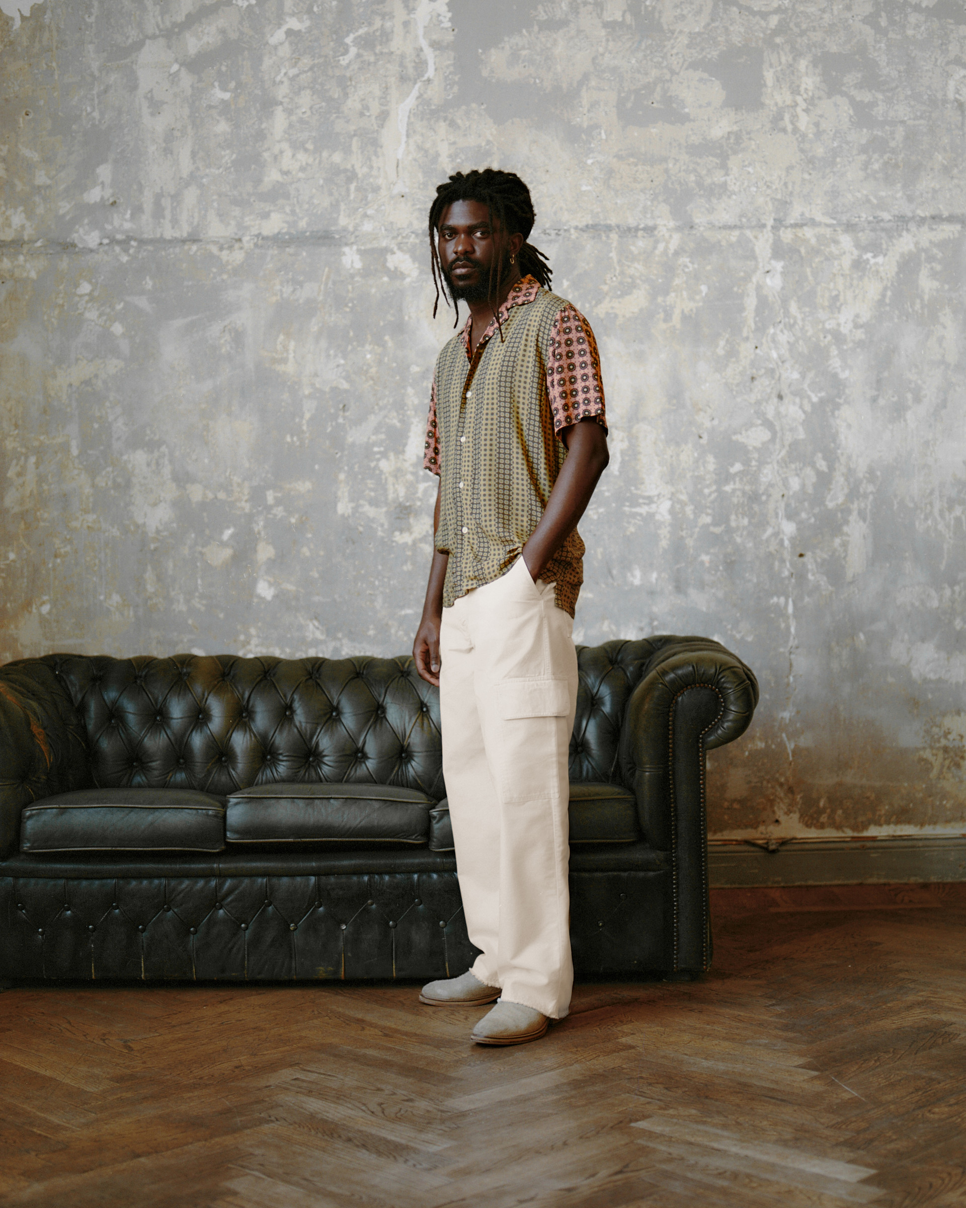 Model in a mixed-print short-sleeve shirt, and ivory cargo trousers against a textured wall.
