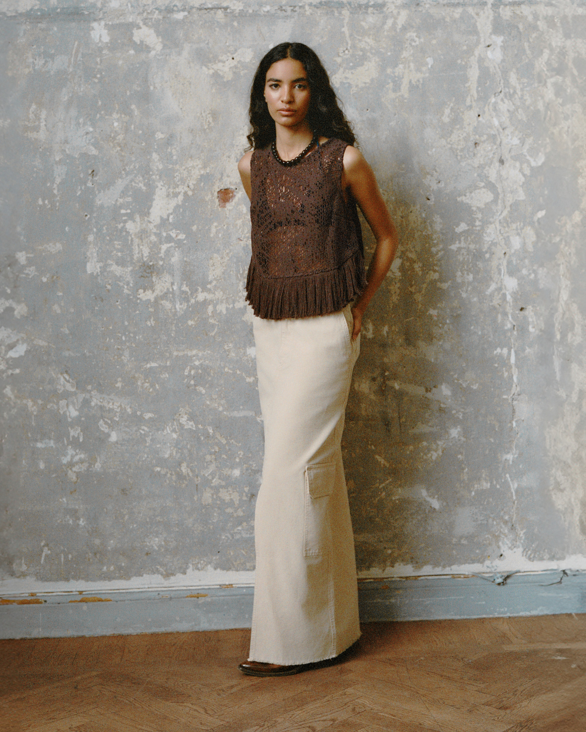 Model in a fringed crochet top, ivory cargo skirt, and leather sandals against a textured wall.